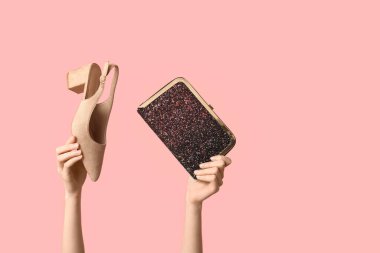 Çantalı kadın elleri ve pembe arka planda topuklu ayakkabılar.