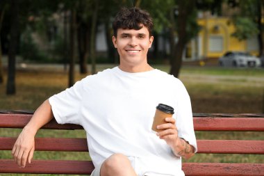 Dışarıda bankta oturan bir fincan lezzetli latte ile yakışıklı genç adam.