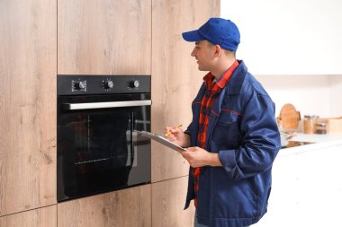 Mutfakta elektrikli fırının yanında panosu olan erkek teknisyen.