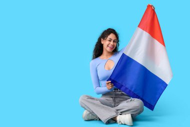 Güzel, genç, mutlu, Afro-Amerikan bayrağı mavi arka planda oturan kadın.