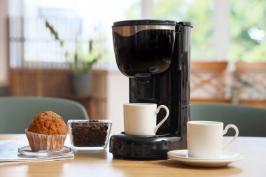 Mutfaktaki kahve makinesinde fincanlar, fasulyeler ve kekler var.