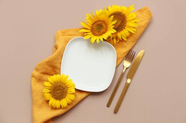 Altın çatal bıçak takımları ve kahverengi arka planda ayçiçekleri olan güzel bir masa.