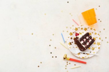 Lezzetli bir dilim doğum günü pastası, fincan ve parti dekoruyla beyaz arka planda