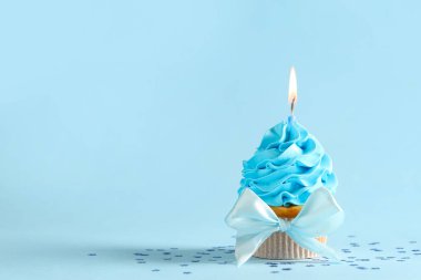 Tatlı doğum günü keki, yanan mum ve mavi arka planda konfeti.