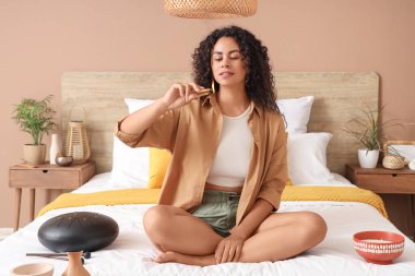 Yanan Palo Santo 'su olan genç Afro-Amerikalı kadın yatak odasında oturuyor.