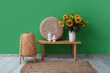 Hasır lambalı şık bir oda ve yeşil duvarın yanında bir vazo ayçiçeği buketi