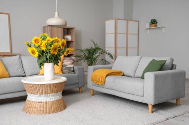 Kahve masasında gri kanepeler ve vazo vazo ayçiçekleri olan şık bir oturma odası.