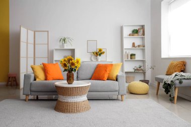 Gri kanepeli şık bir oturma odası ve kahve masasında ayçiçeği buketleri.