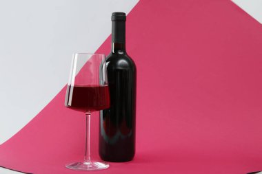 Renkli arka planda bir şişe kırmızı şarap ve bardak.