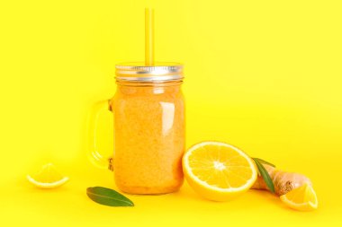 Sarı arka planda saman bulunan sağlıklı portakal suyu kavanozu.
