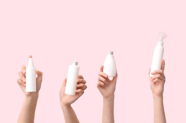 Pembe arka planda farklı kozmetik ürünleri olan kadın elleri