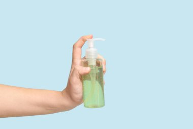 Mavi arka planda kozmetik ürünü şişesi olan bir kadın el.