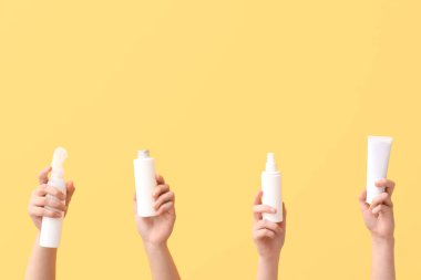 Sarı arka planda farklı kozmetik ürünleri olan kadın elleri