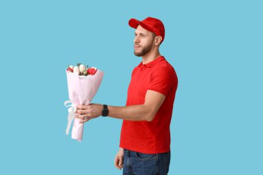 Mavi arka planda bir buket güzel lalesi olan genç teslimatçı.