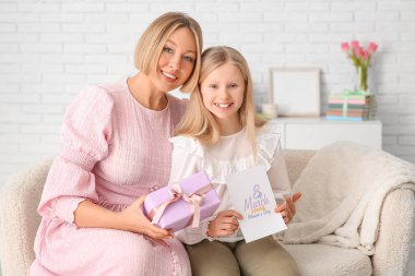 Elinde hediye kutusu olan güzel bir genç kadın ve oturma odasındaki kanepede oturan küçük tatlı kızı.