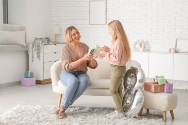 Elinde hediye kutusu olan genç ve güzel bir kadın ve oturma odasında balon şeklinde bir bedeni olan küçük tatlı kızı.