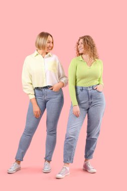 Pembe arka planda şık kotlu güzel mutlu kadınlar.