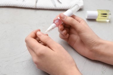 Gri grunge arka planda tırnaklarına tırnak yağı süren kadın elleri, yakın plan.