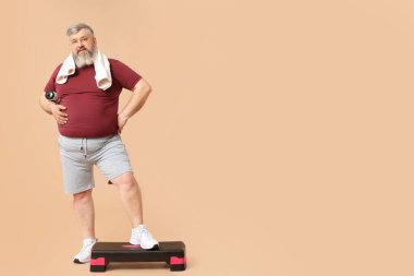 Aşırı kilolu, aerobik basamaklı ve bej arka planda bir şişe suyu olan olgun bir adam. Kilo verme konsepti