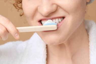 Güzel genç bir kadın, kahverengi arka planda dişlerini fırçalıyor.