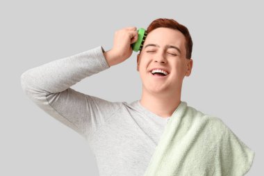 Genç adam gri arka planda saç derisi masaj aleti kullanıyor.