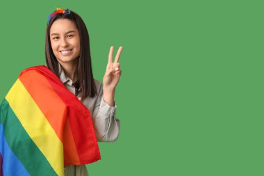 Yeşil arka planda zafer jesti gösteren LGBT bayrağıyla güzel genç bir kadın.