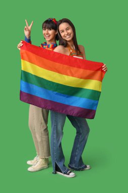 LGBT bayrağıyla genç lezbiyen çift yeşil arka planda zafer jesti gösteriyor