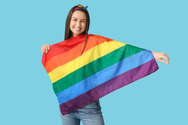 Mavi arka planda LGBT bayrağı olan mutlu genç bir kadın.