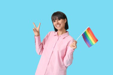 Mavi arka planda zafer jesti gösteren LGBT bayrağıyla güzel genç bir kadın.