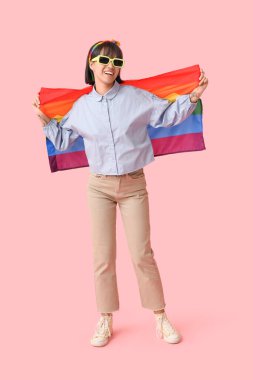 Pembe arka planda LGBT bayrağı olan güneş gözlüklü mutlu genç bir kadın.