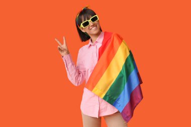 Turuncu arka planda zafer jesti gösteren LGBT bayrağıyla güzel genç bir kadın.
