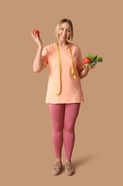 Bej arka planda mezurası ve taze sebzeleri olan genç ve güzel bir bayan. Kilo verme konsepti