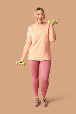 Güzel bir genç bayan, bej arka planda halterlerle egzersiz yapıyor. Kilo verme konsepti