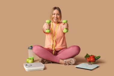 Bej arka planda farklı pulları ve dambılları olan güzel bir genç kadın. Kilo verme konsepti