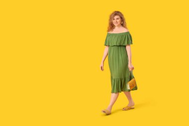 Sarı arka planda zincir çantalı şık yeşil elbiseli güzel bir kadın.