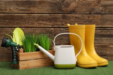 Sulama kabı, lastik bot ve su püskürtücüsü ile yeşil çimlerin üzerine ahşap arka planda kompozisyon