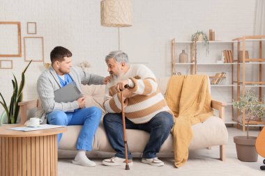 Genç bakıcı evde yaşlı bir adamla ilgileniyor.