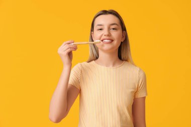 Sarı arka planda diş fırçası olan genç bir kadın.