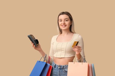 Kredi kartı, ödeme terminali ve bej arka planda alışveriş torbaları olan genç bir kadın.