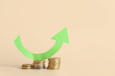 Bej arkaplan üzerinde ok olan bozuk para yığınları. Fiyat artışı kavramı