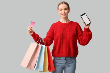 Kredi kartı, cep telefonu ve arka planda alışveriş torbaları olan genç bir kadın.