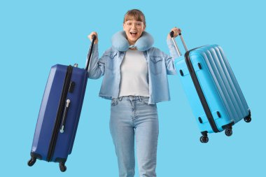 Güzel, genç, mutlu bayan turist bavulları ve mavi arka planda seyahat yastığı.