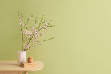 Çiçek açan dalları, kitapları ve hava nemlendiricisi olan vazolar yeşil duvarın yanındaki ahşap masada.