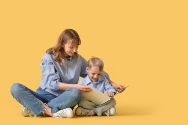 Mutlu anne ve küçük oğlu sarı arka plan üzerine kitap okuyorlar.