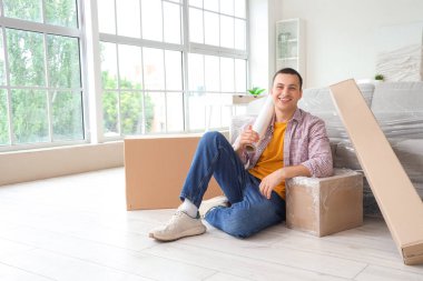 Geniş ambalajlı ve kutularla evde oturan genç adam.