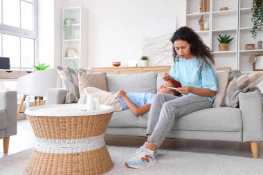 Termometresi olan Afro-Amerikalı bir anne evinde oğlunun alnına dokunuyor.