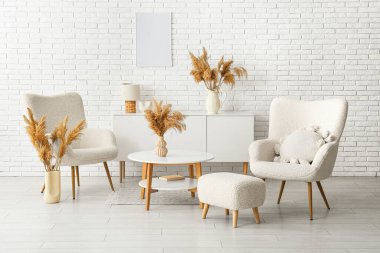 Oturma odasındaki beyaz tuğla duvarın yanında kuru kamışlı vazolar.