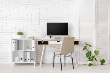 Ofisteki beyaz tuğla duvarın yanındaki masada modern elektrikli vantilatör.