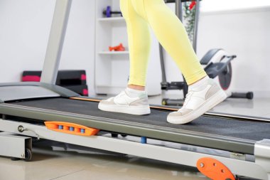 Spor salonundaki koşu bandında spor yapan kadın, yakın plan.