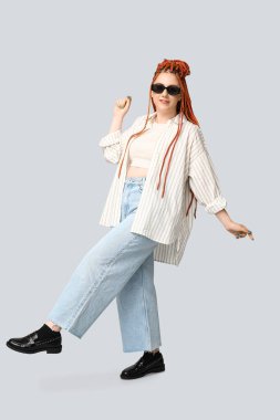 Gri arka planda rastaları olan zarif genç bir kadının portresi.